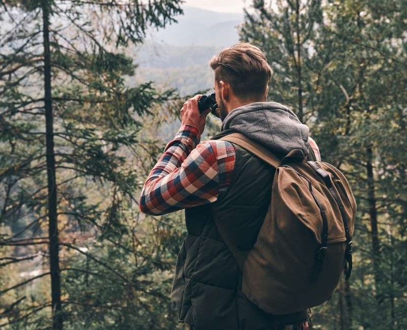 Mann som ser med kikkert utover naturlandskap